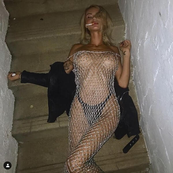 sahara_ray, sexy Instagram model, wears fishnet dress and lies on the ground while smoking.